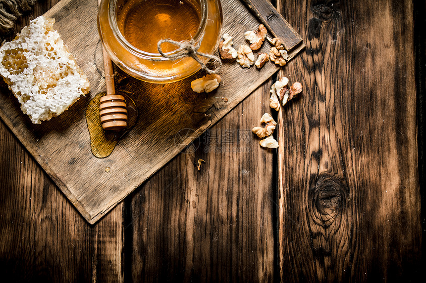 蜂蜜背景梳子里的甜蜂蜜有坚果的玻璃罐子木头背景的甜蜜梳子里有坚果玻璃罐子图片