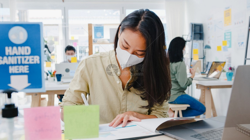 作为商业女企家身戴医疗面罩在新的正常情况下在预防方面保持社会偏移同时在办公室工作使用笔记本电脑在科罗纳后生活和工作图片