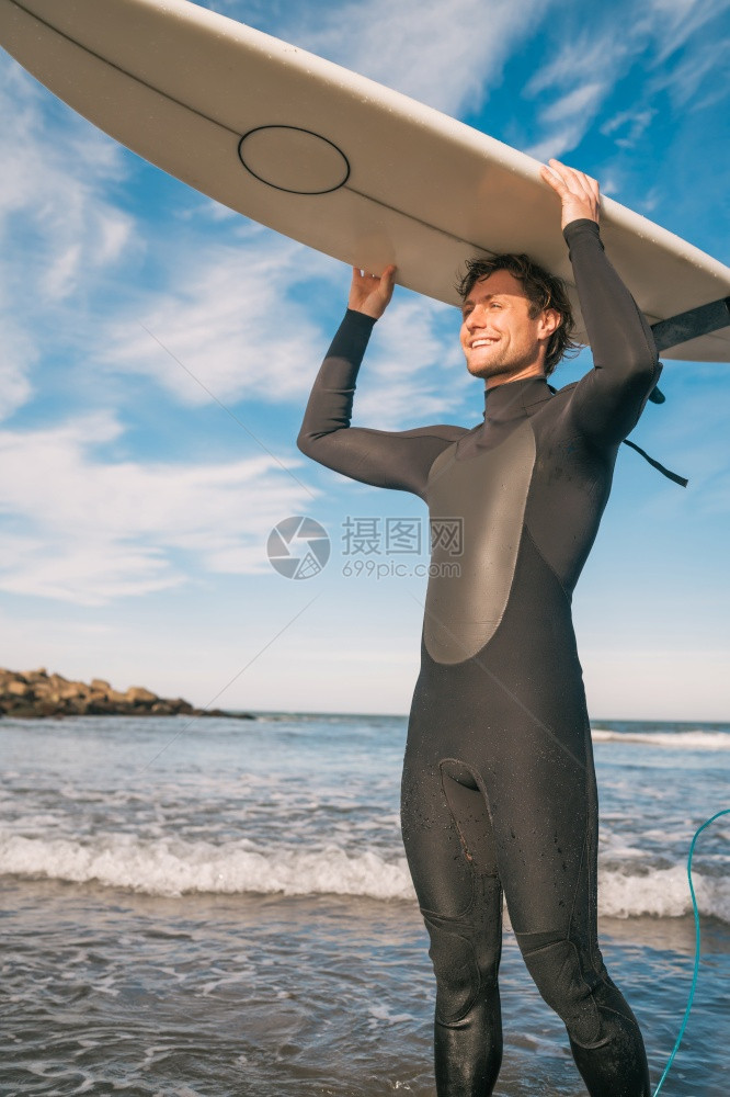 海滩上年轻冲浪手的肖像举起他冲浪板穿着黑色冲浪西装运动和水上的概念图片