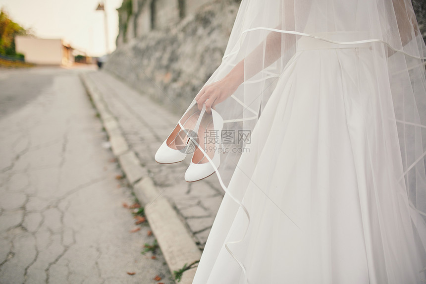 身着婚纱和面的新娘带着鞋子走在街上图片