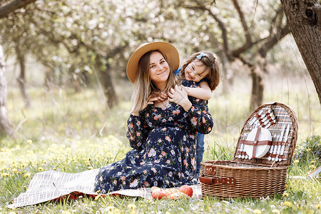 美丽的孕妇与女儿一起在盛开的春天花园野餐上玩耍图片