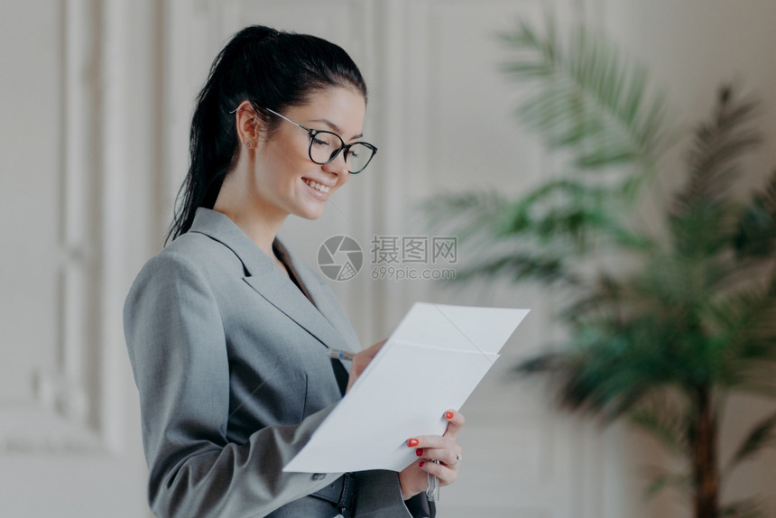 很高兴女律师在公司纸质文件中写道戴光学眼镜穿正规衣服站在自己的内阁里制定新的战略拥有快乐的表达方式图片