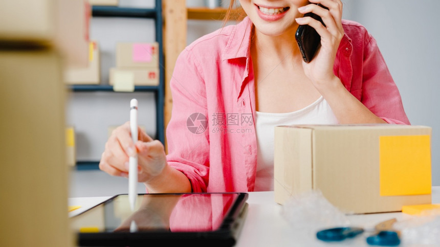 利用移动电话接收定购单和检查库存产品在家庭办公室工作小企业主在线市场交付自由职业者生活方式概念的年轻女商人图片