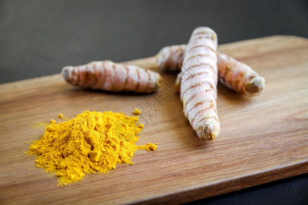 姜黄色木砧板上的姜黄根和香料粉姜黄根和香料粉放在砧板上背景