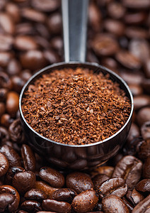 在咖啡豆上方黑钢勺中的新鲜生有机土咖啡粉背景图片