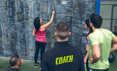运动员妇女与同学和教练一起在体育场的黑板上写成绩图片