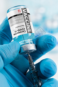 灵丹妙药医生或护士佩戴外科手套持罗纳cornaviuscovid19疫苗瓶和注射器背景