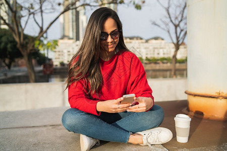 短讯年轻美女坐在户外时使用手机的肖像背景