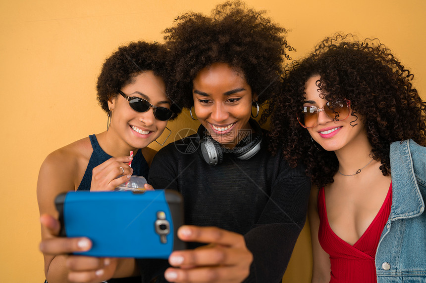 三个朋友用手机自拍反黄墙科技友谊和生活方式概念图片