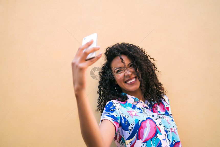 年轻for女人用手机自拍与黄色墙对着技术概念图片