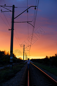 女孩徒步旅行者站在日落的光下站在铁路上图片