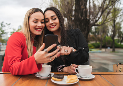 两位年轻朋友坐在咖啡店时使用手机的肖像图片