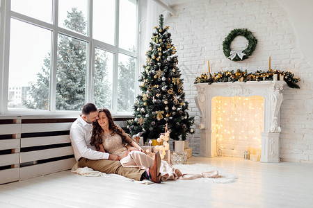 一对夫妻坐在圣诞树旁拥抱亲吻图片