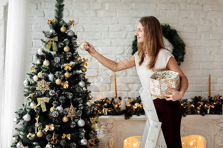 有壁炉和许多礼物喜笑的少女在工作室白砖墙背景上装饰圣诞树背景图片
