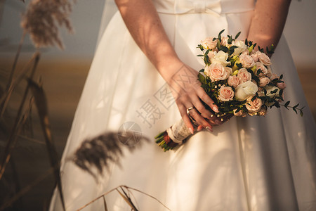 新娘穿着优雅的婚纱盛着一束美丽的花朵和绿色叶子婚礼主题穿着优雅的婚纱新娘拿着一束美丽的花朵和绿色叶子背景图片