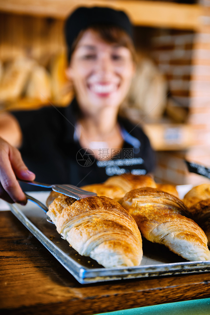 身穿黑色制服卖羊角面包的美丽而微笑女面包店助理图片