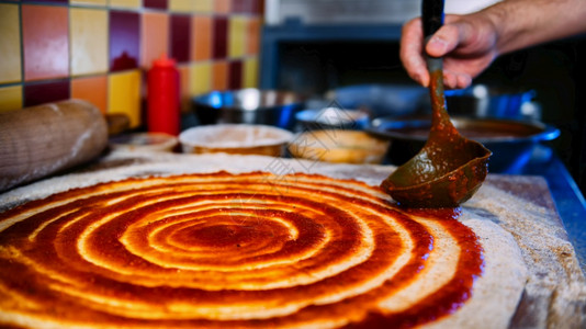 厨师在比萨饼面团上撒番茄酱披萨餐厅的金属拉链披萨制作过程图片