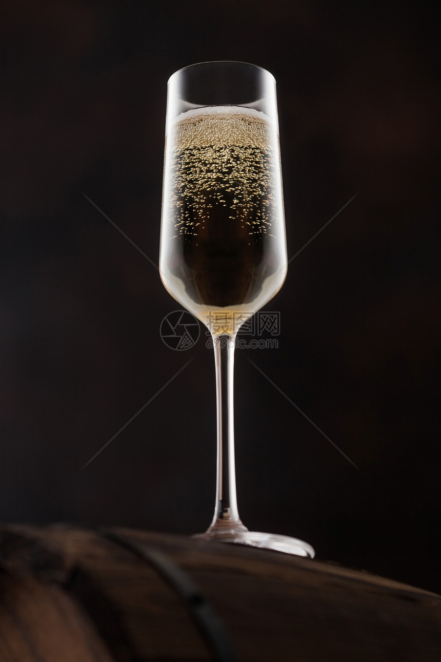 玻璃香槟的泡沫在木桶顶部黑色背景的木桶图片