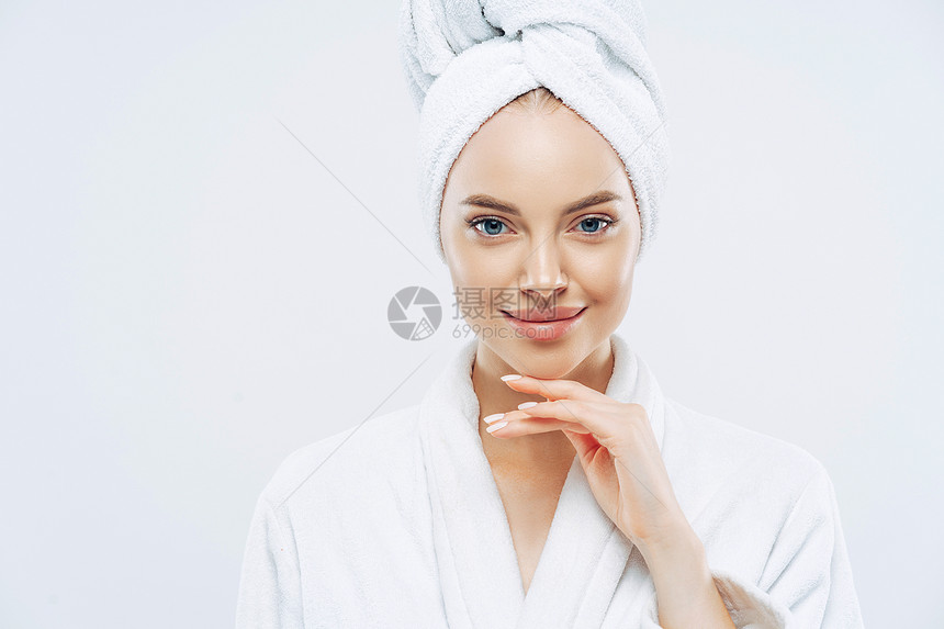 年轻英俊的欧洲女脸色平和享受洗浴程序穿着软白袍头部毛巾与白背景隔绝清晨卫生图片