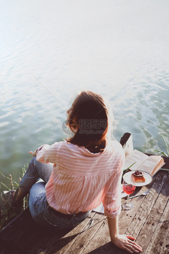 女孩在光亮的夏季河岸木码头上享受野餐图片