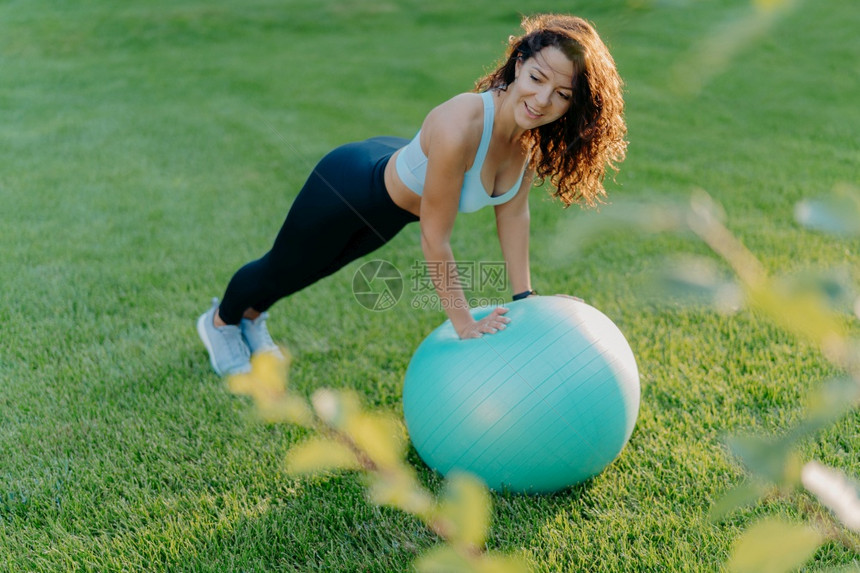 健美的瘦女人靠在合身的球上穿着积极服饰在绿草坪上进行体操练习享受运动和最喜欢的活引导健康的生活方式人有氧运动健身概念图片