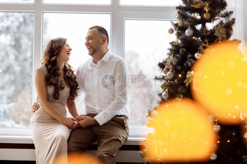 一对夫妻坐在圣诞树旁的窗户上愉快大笑图片