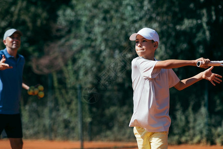 网球教官男孩在粘土场上有网球课教官和男孩在网球课上有教官图片