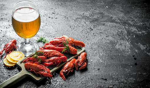 煮熟的龙虾在切口板上面有啤酒和柠檬片黑色生锈背景图片