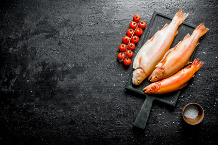 生鱼鳟在切菜板上树枝有西红柿碗里盐黑色生锈背景鱼鳟在切菜板上碗里有盐图片