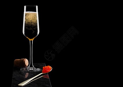 优雅的黄色香槟杯子红鱼酱放在金勺上鱼子酱瓶放在大理石板上黑图片