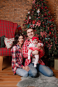 圣诞节前夕的幸福家庭在客厅父亲母和女婴的装饰树旁坐在一起庆祝新年假期的概
念圣诞节前夕的幸福家庭在客厅母亲和女婴的装饰树旁坐在一背景图片