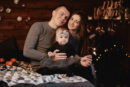 可爱的年轻家庭父亲妈和小姑娘床上有火花和圣诞节背景后面有圣诞背景图片