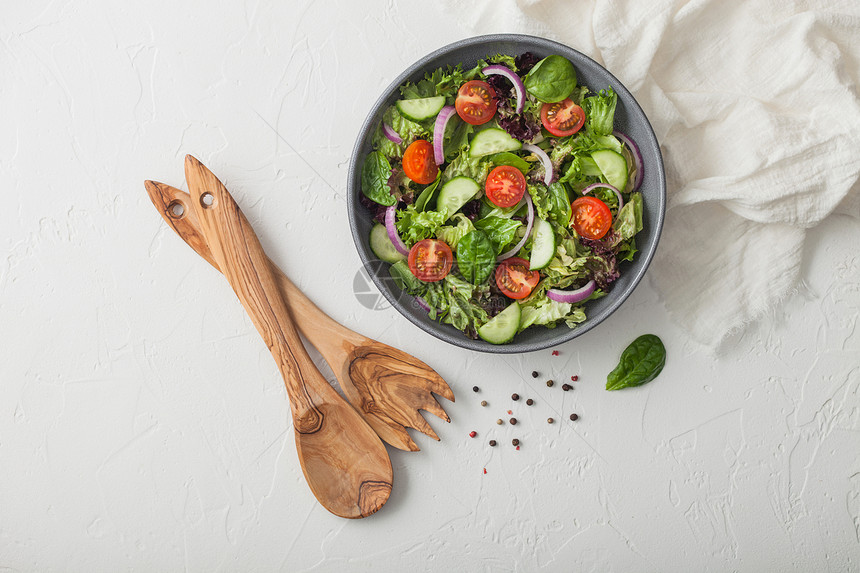 新鲜健康的素食蔬菜沙拉配有生和西红柿洋葱以及白桌底灰色碗盘中的菠菜配有叉子和勺图片