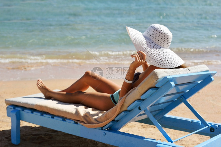 在热带旅行度假胜地的海滩上晒太阳享受暑假女孩用手戴帽子在靠近海边的遮太阳员身上美丽的女人在热带旅行度假胜地的海滩上晒太阳享受暑假图片