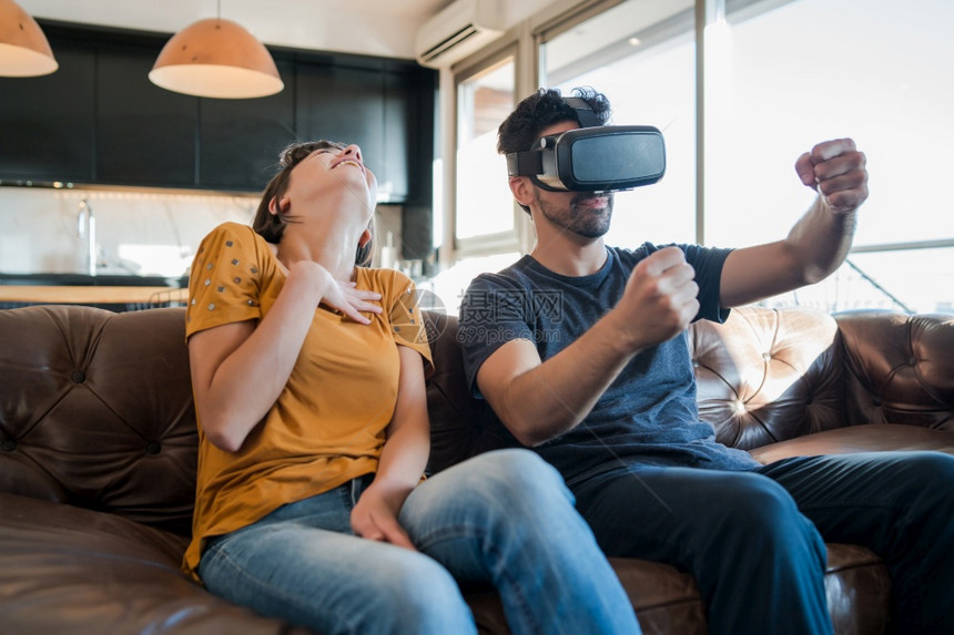 一对年轻夫妇起玩游戏坐在沙发上时用vr眼镜玩电子游戏新的正常生活方式概念图片