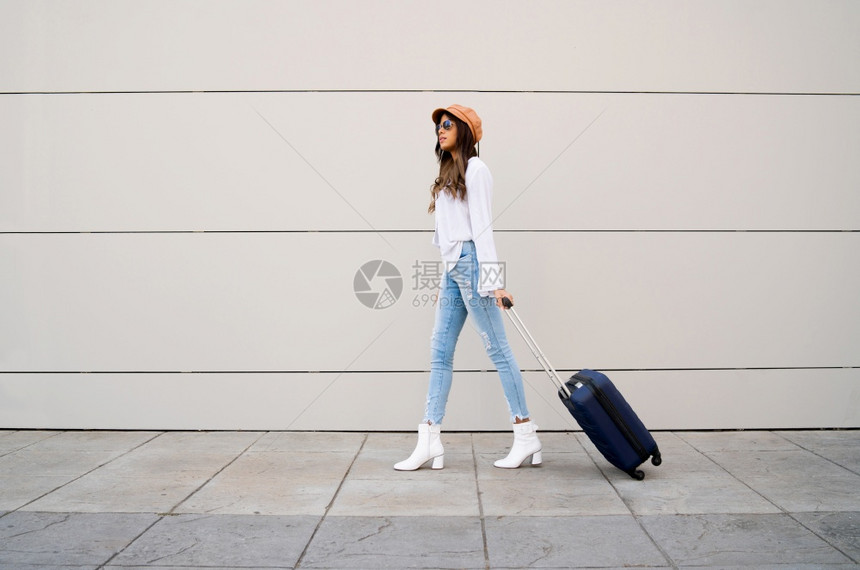 年轻旅行者女子在街上户外散步时携带手提箱的肖像图片
