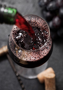 将红酒从瓶子倒到杯上以黑色背景装有瓶子和最高视图图片