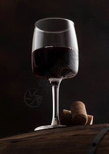 一杯红葡萄酒木桶顶上有软塞在黑色背景的木桶上图片