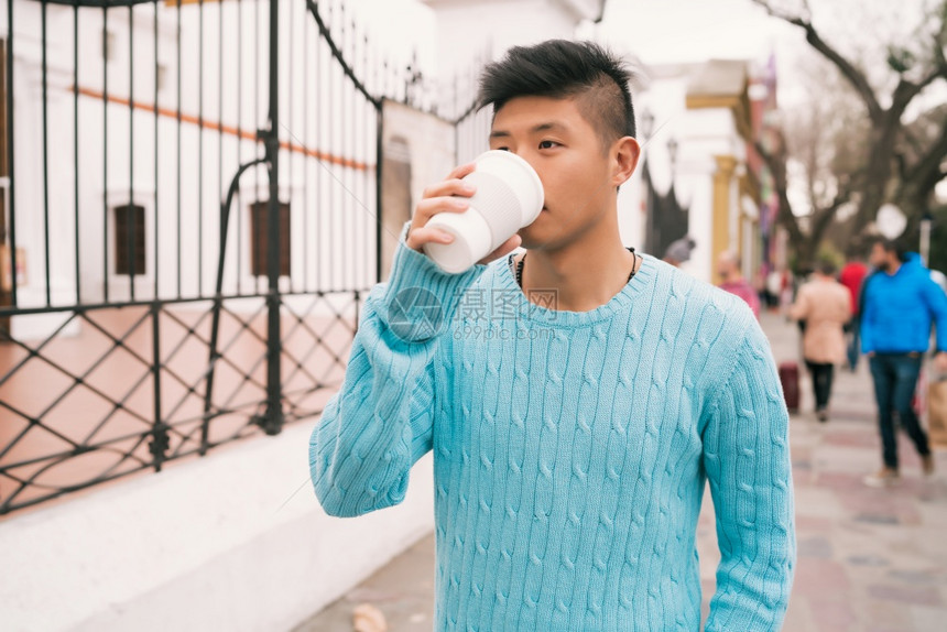 年轻亚洲男子在街上户外散步时喝咖啡的肖像图片