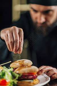 男厨在餐厅做饭装饰素食汉堡与下降的芝麻厨师在餐厅做装饰素食汉堡与芝麻图片