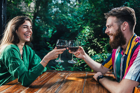 一对夫妇在约会时笑着喝红酒年轻男女坐在木桌旁穿着丰富多彩的服装图片