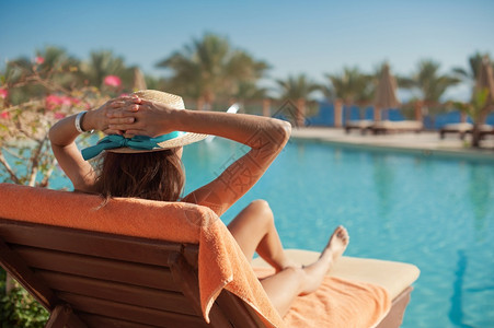 日光浴床穿着草帽的女子在豪华夏日泳池酒店附近的日睡床上放松概念旅行时间背景