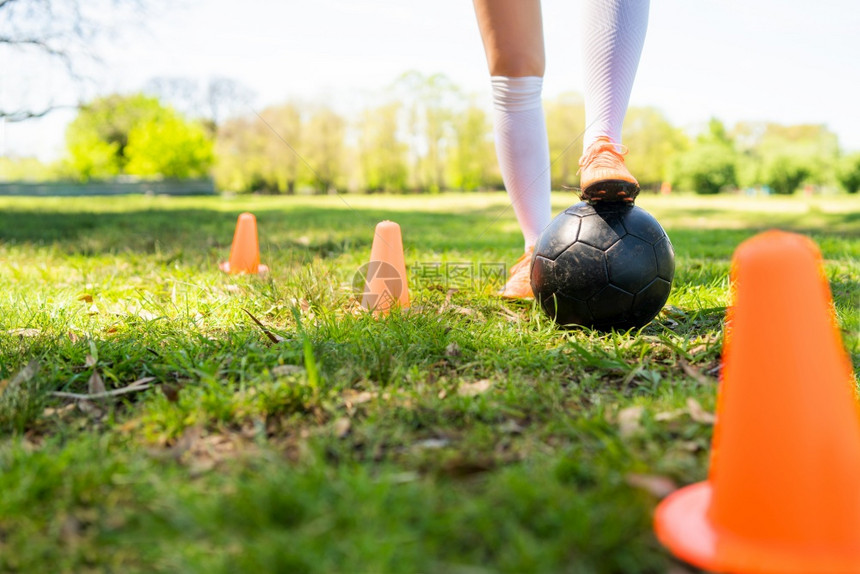 年轻女足球运动员在田野上练习球时环绕锥子跑动的肖像图片