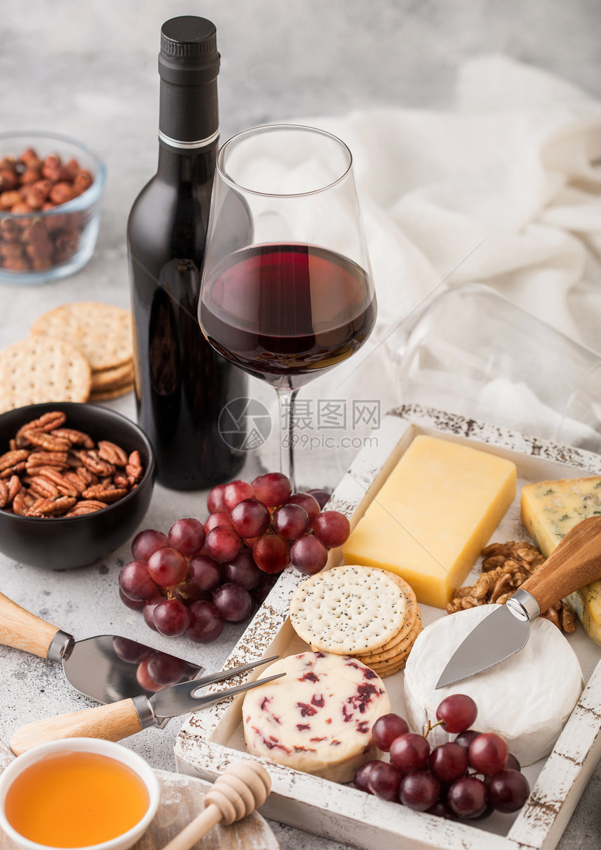 红葡萄酒瓶和杯在木箱中挑选各种奶酪和浅底的葡萄图片