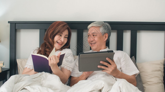 亚裔老人夫妇在家里使用平板电脑亚裔老人祖父母丈夫看电影妻子醒来后看书图片