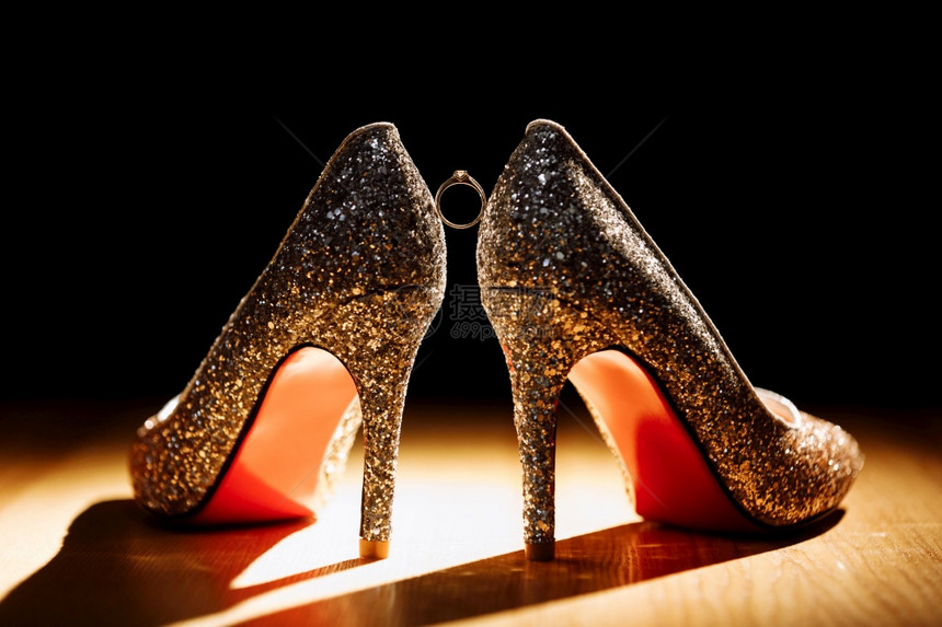 金色戒指在深背景的一双新娘鞋之间有选择的焦点金色戒指黑背景的一对新娘鞋之间有选择的焦点图片