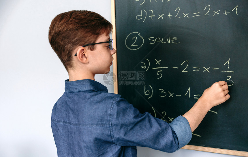 男孩在学校的黑板上解答数学练习图片