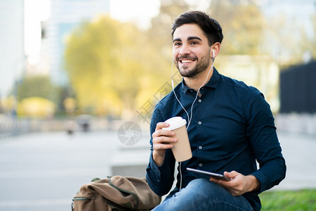 年轻人用数码平板电脑画像坐在户外的长椅上并举杯咖啡城市概念图片