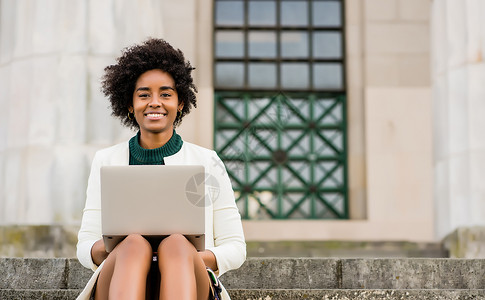 afro商业妇女坐在户外楼梯上时使用她的笔记本电脑城市和商业概念图片