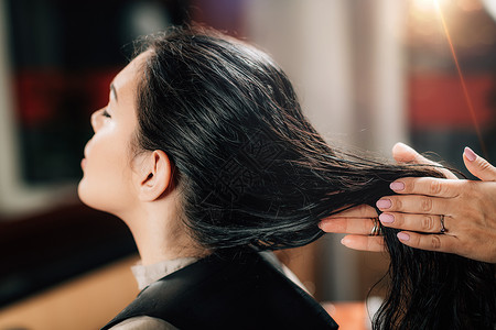 将恢复的油滴应用到妇女身上的理发师和长的黑头发型师将恢复的油滴应用到妇女身上理发师背景图片